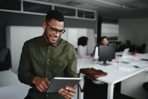 Successful smiling young man in office using digital tablet