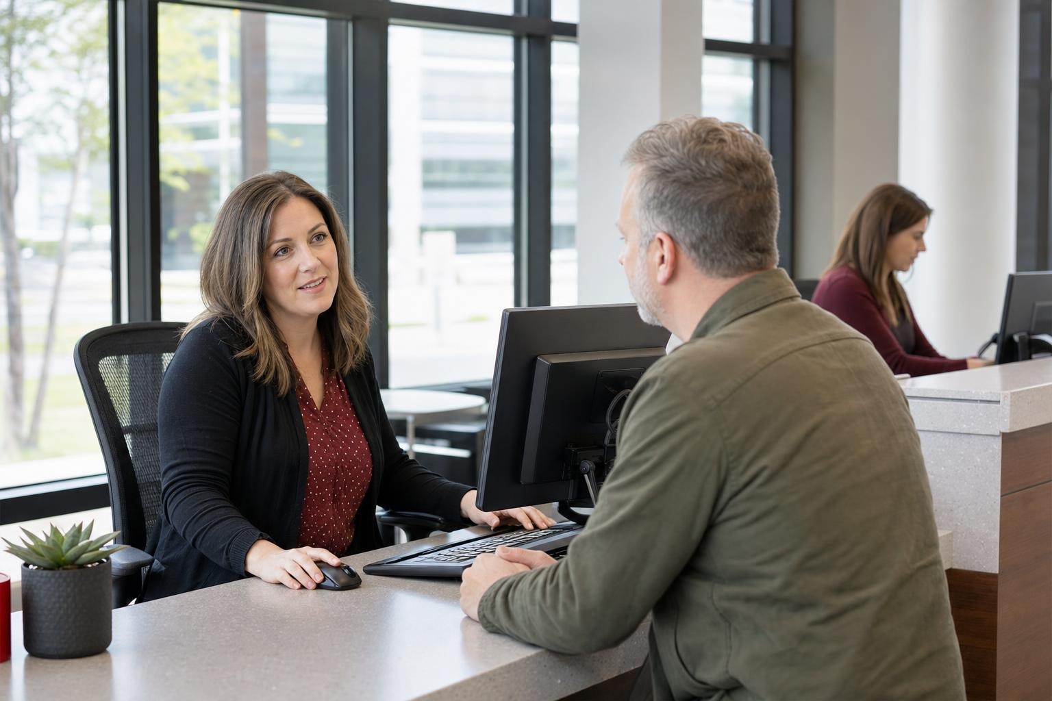 Staff member assists a resident at a public-service counter with office workstations.